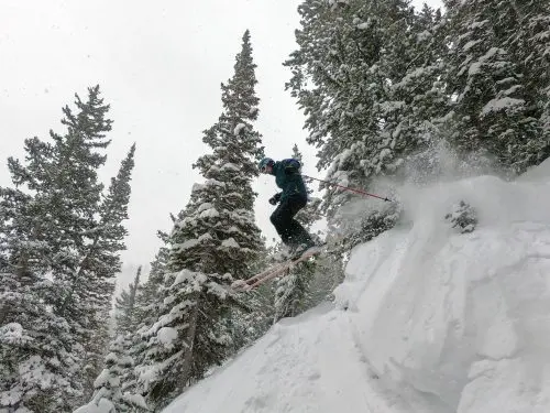 man jumping off cliff with skis